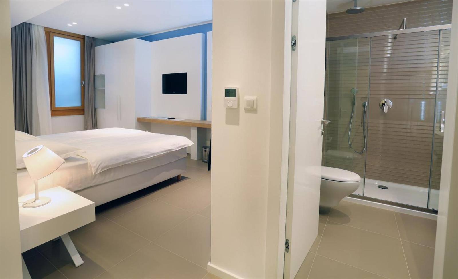 Bedroom with a view into the glass-enclosed shower and bathroom