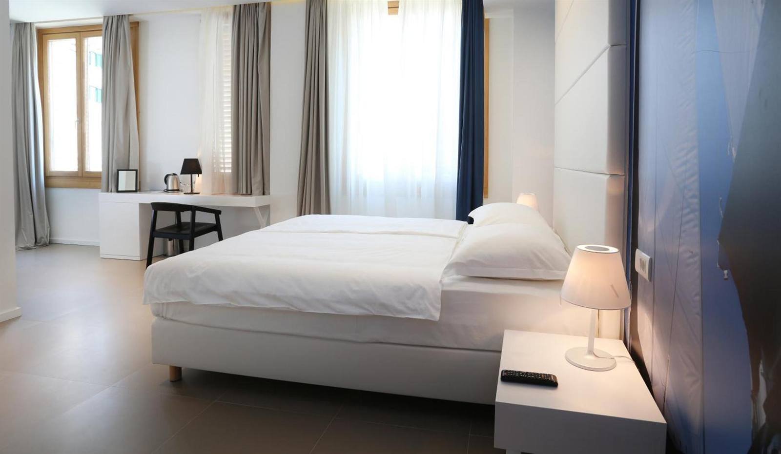 Bright double bedroom with large windows and a bedside lamp